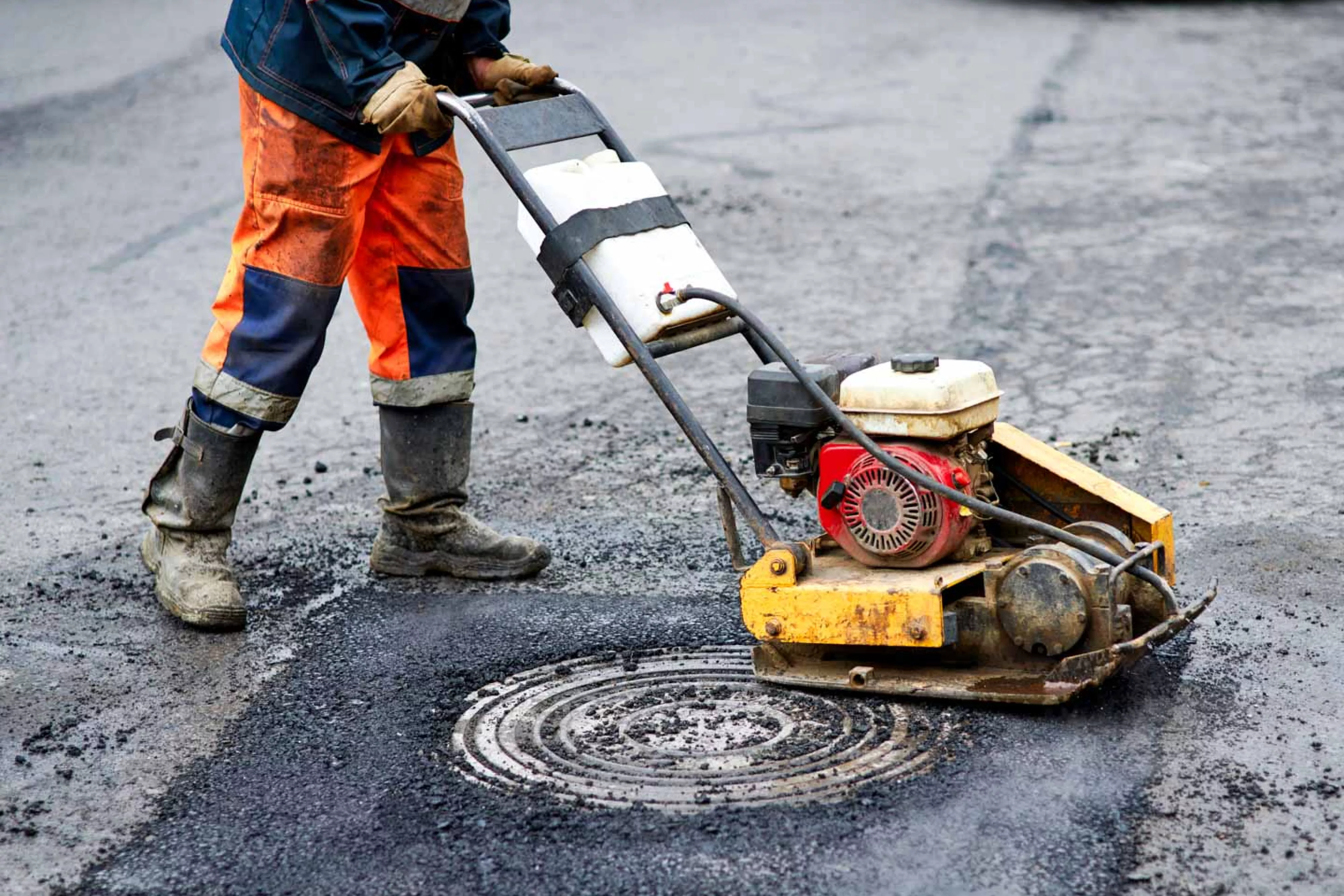 Road crew worker uses machine to press asphalt