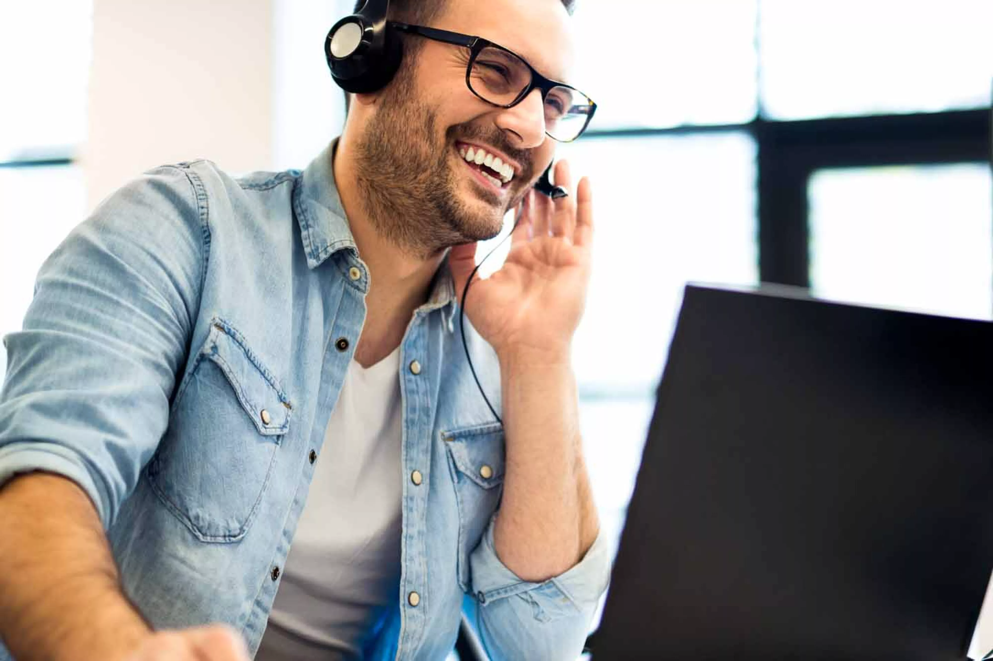 Smiling man with headset works at laptop