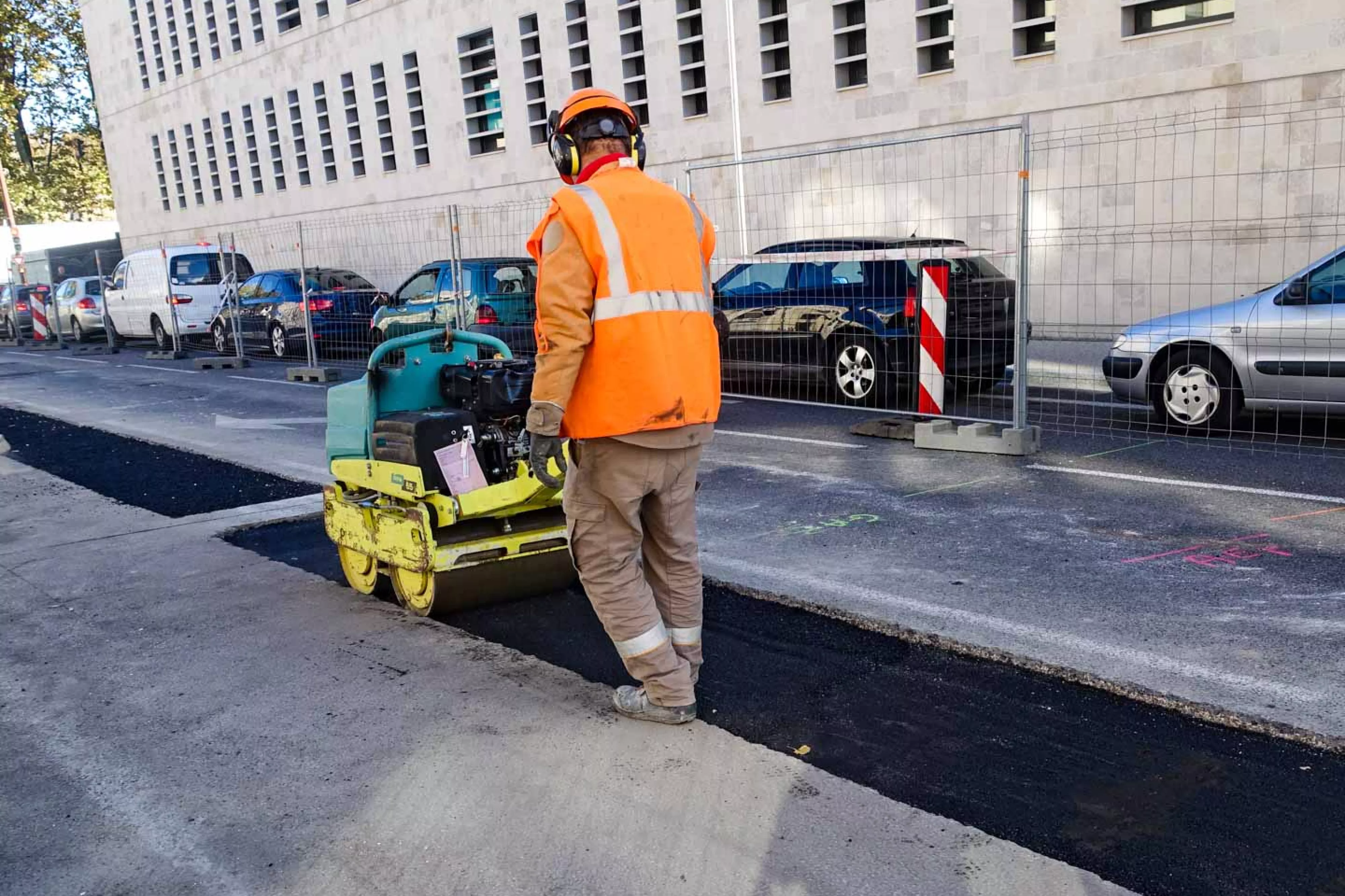 Member of road crew uses machine to flatten new asphalt