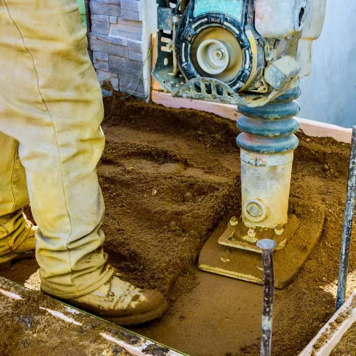 Construction worker uses vibratory hammer in dirt
