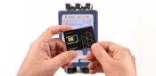 Holding a SIM card with the Micromate Plus in the background.